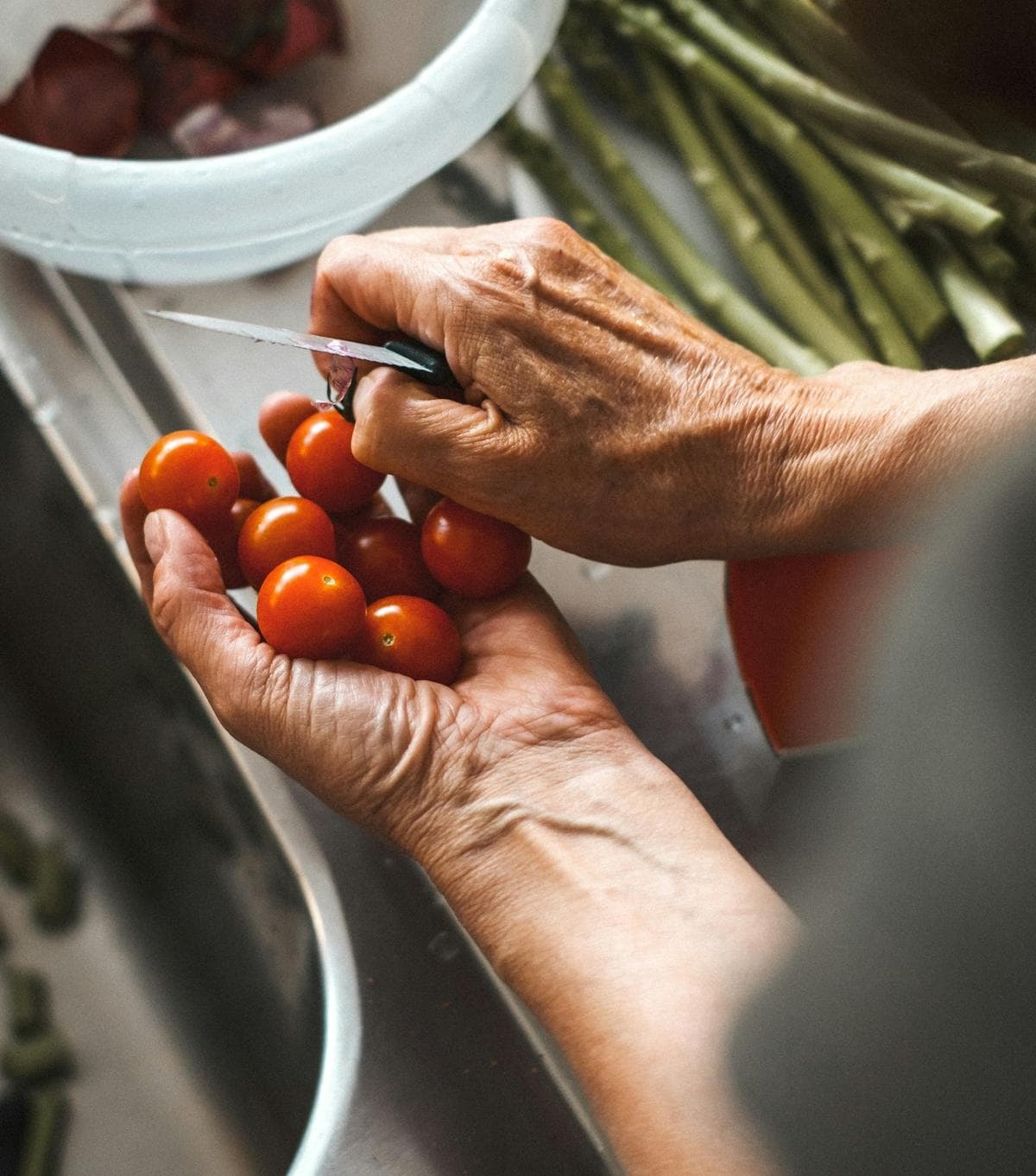Hands slicing cherry tomatoes over a bowl of greens.